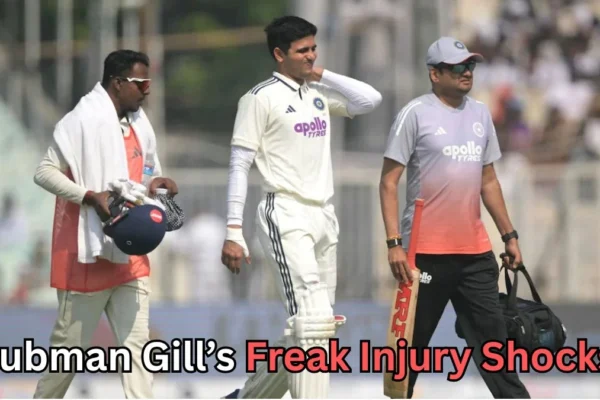 A male cricket player in a white uniform walks off the field holding his face in apparent discomfort, accompanied by two support staff members dressed in training gear. One staff member carries a helmet and towel, while the other carries a bat and a kit bag. The scene appears to take place during a match, with spectators blurred in the background. Text at the bottom reads: “Shubman Gill’s Freak Injury Shocks?”A male cricket player in a white uniform walks off the field holding his face in apparent discomfort, accompanied by two support staff members dressed in training gear. One staff member carries a helmet and towel, while the other carries a bat and a kit bag. The scene appears to take place during a match, with spectators blurred in the background. Text at the bottom reads: “Shubman Gill’s Freak Injury Shocks?”