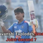 A young cricketer wearing an Indian team jersey raises his bat and helmet in celebration after a significant achievement. The player, likely a junior or emerging talent, smiles as he acknowledges the crowd. The background features empty seats in a stadium. Text at the bottom reads: "Suryavanshi Explodes Smashes Joint-Second?