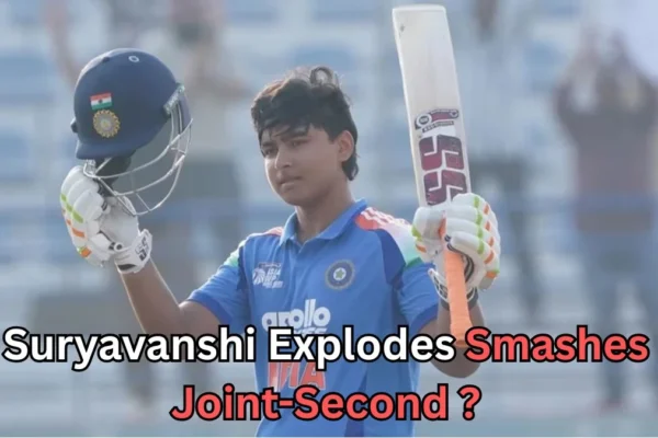 A young cricketer wearing an Indian team jersey raises his bat and helmet in celebration after a significant achievement. The player, likely a junior or emerging talent, smiles as he acknowledges the crowd. The background features empty seats in a stadium. Text at the bottom reads: "Suryavanshi Explodes Smashes Joint-Second?
