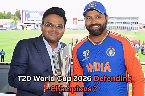 A man in a dark suit holding a cricket trophy stands beside a man wearing an India T20 cricket jersey and cap. Both are smiling at the camera inside a cricket stadium. Text on the image reads: “T20 World Cup 2026 Defending Champions?”