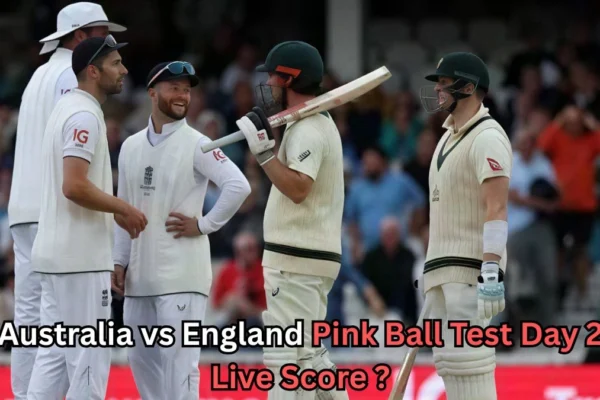 England fielders and two Australian batters stand together on the cricket field during the Ashes pink-ball Test, appearing to share a light moment, with text overlaid asking for the Australia vs England Pink Ball Test Day 2 live score.