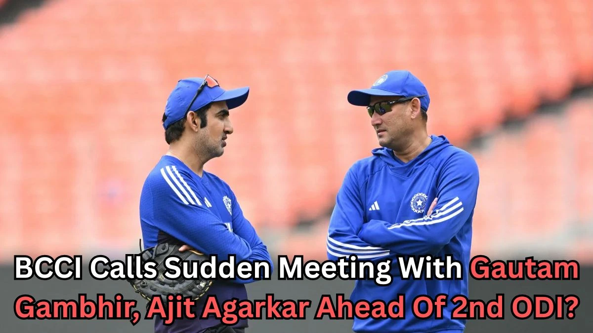 Two men wearing blue training outfits and caps are standing on a cricket field, engaged in conversation. They appear to be part of the Indian cricket setup. The background shows empty orange stadium seats. Text on the image reads: “BCCI Calls Sudden Meeting With Gautam Gambhir, Ajit Agarkar Ahead Of 2nd ODI?