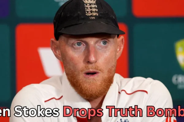 A man with a reddish beard wearing a black cricket cap and a white cricket uniform speaks at a press conference. Behind him is a backdrop with sports logos and red and green panels. Text at the bottom of the image reads “Ben Stokes Drops Truth Bomb?
