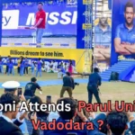 A large crowd gathers at an outdoor event where a well-known cricketer appears on stage at Parul University in Vadodara. Huge screens display his image, including one showing him holding a cricket bat and another showing him posing with folded arms. Many people in the audience are taking photos and videos. Text on the image reads: “MS Dhoni Attends Parul University Vadodara?